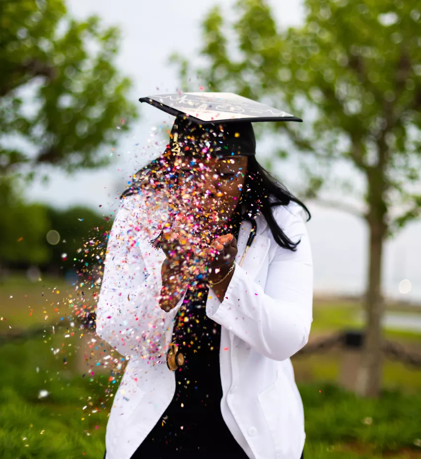 Female student on graduation day blowing confetti. Photo.