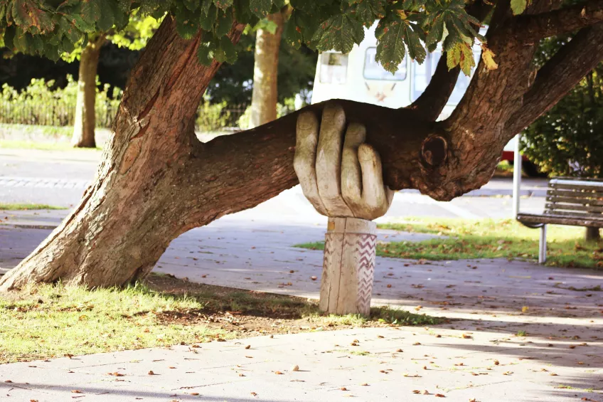 Sculpture in shape of a huge hand holds up a real tree branch. Photo.